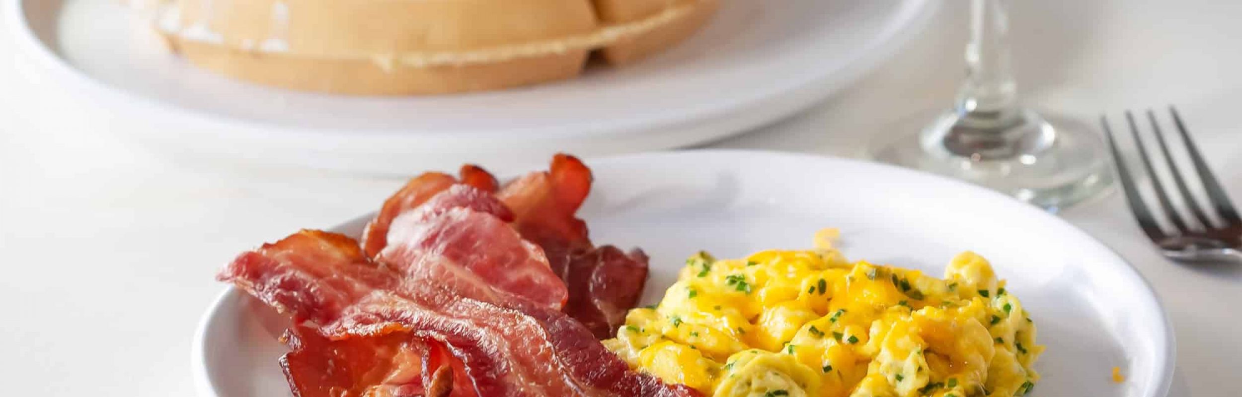 Focus on Bacon and Eggs on a Plate in Front of a Plate of Waffles